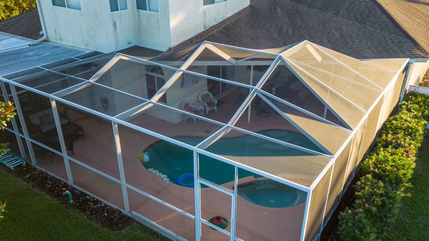 A backyard pool and patio protected by a modern screen enclosure, blending outdoor living with comfort and bug-free relaxation.